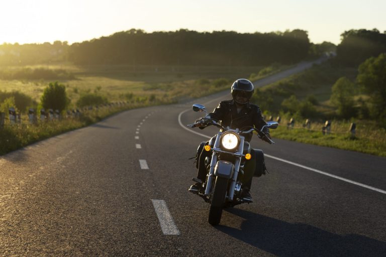 Man riding motorcycle with green hills and tress in the background illustrates blog "Is Motorcycle Insurance Less Expensive Than Car Insurance?"