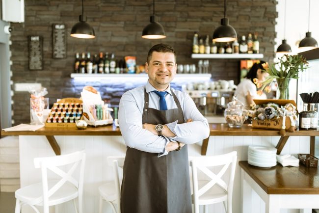 small-business-owner-fp Man with folded arms in small business establishment illustrates blog "Does Commercial Property Insurance Cover Roof Leaks?"