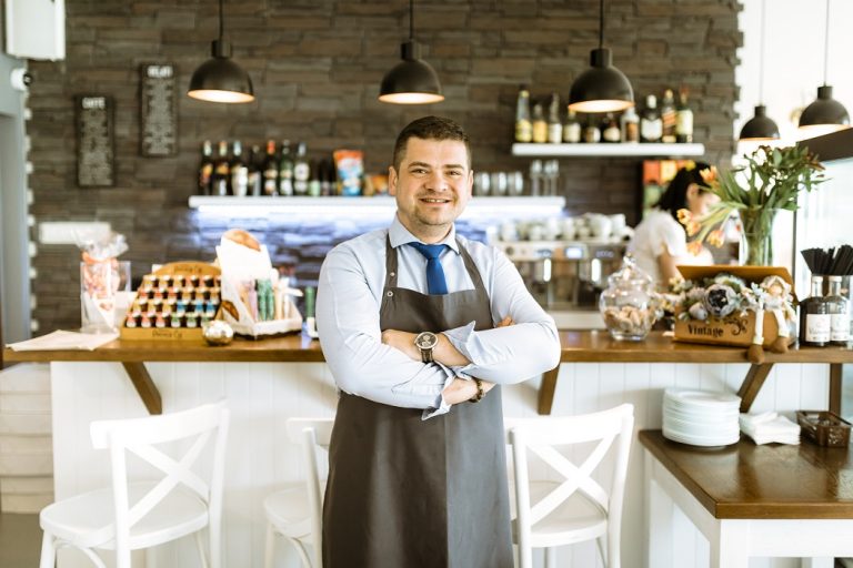 Man with folded arms in small business establishment illustrates blog "Does Commercial Property Insurance Cover Roof Leaks?"