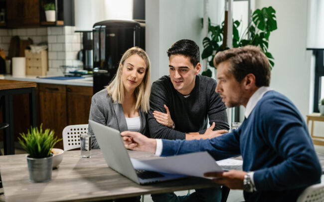 young-couple-real-estate-agent-using-laptop-while-going-through-housing-plan-meeting