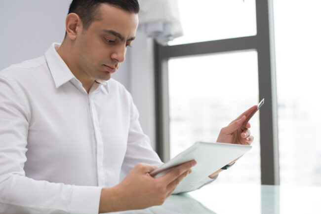 Portrait of serious young businessman working on digital tablet Business owner reviewing insurance audit checklist